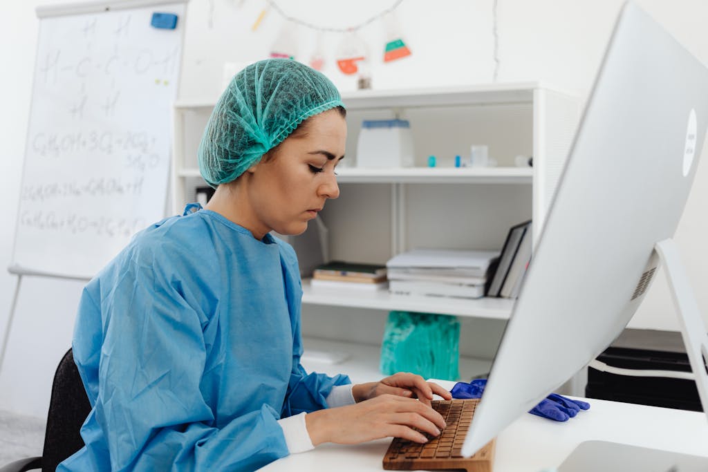 Woman in Blue Scrub Suit Typing on a Wooden Keyboard