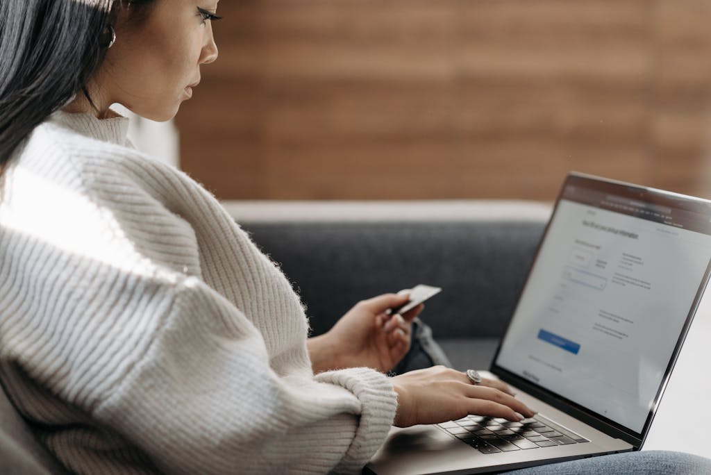 Woman sitting on a couch, shopping online using a laptop and a credit card.